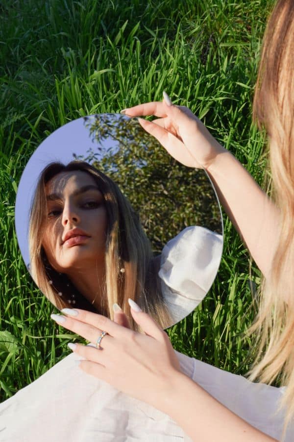 You Should Talk to Yourself Like Someone You Love! 1 young woman looking in a mirror outside in the grass
