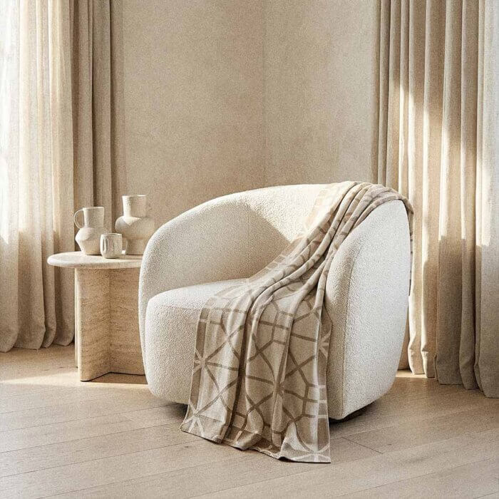ream cotton throw blanket draped on cream upholstered armchair with warm minimalist living room styling