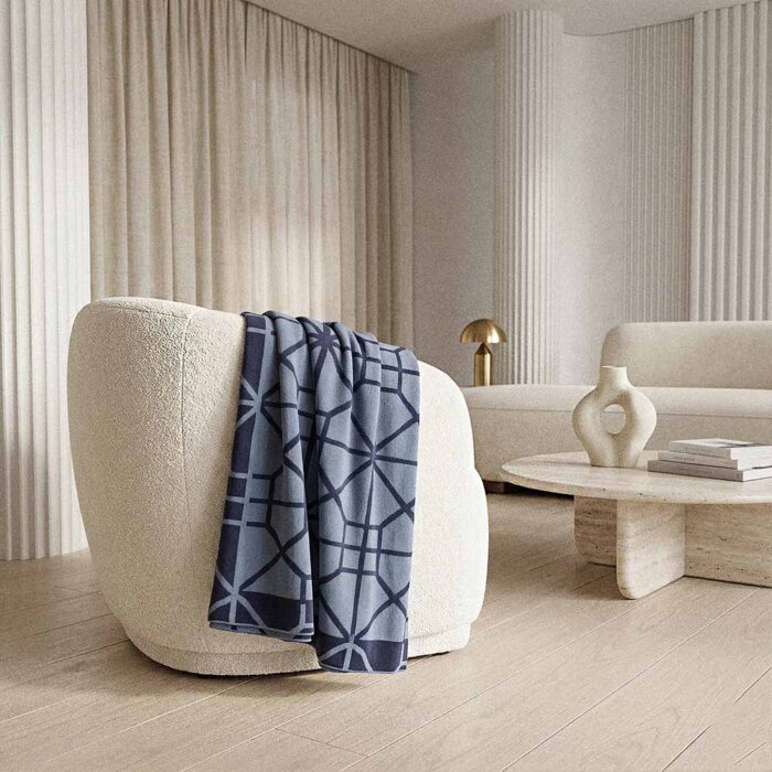 navy cotton throw blanket draped on cream upholstered armchair with warm minimalist living room styling