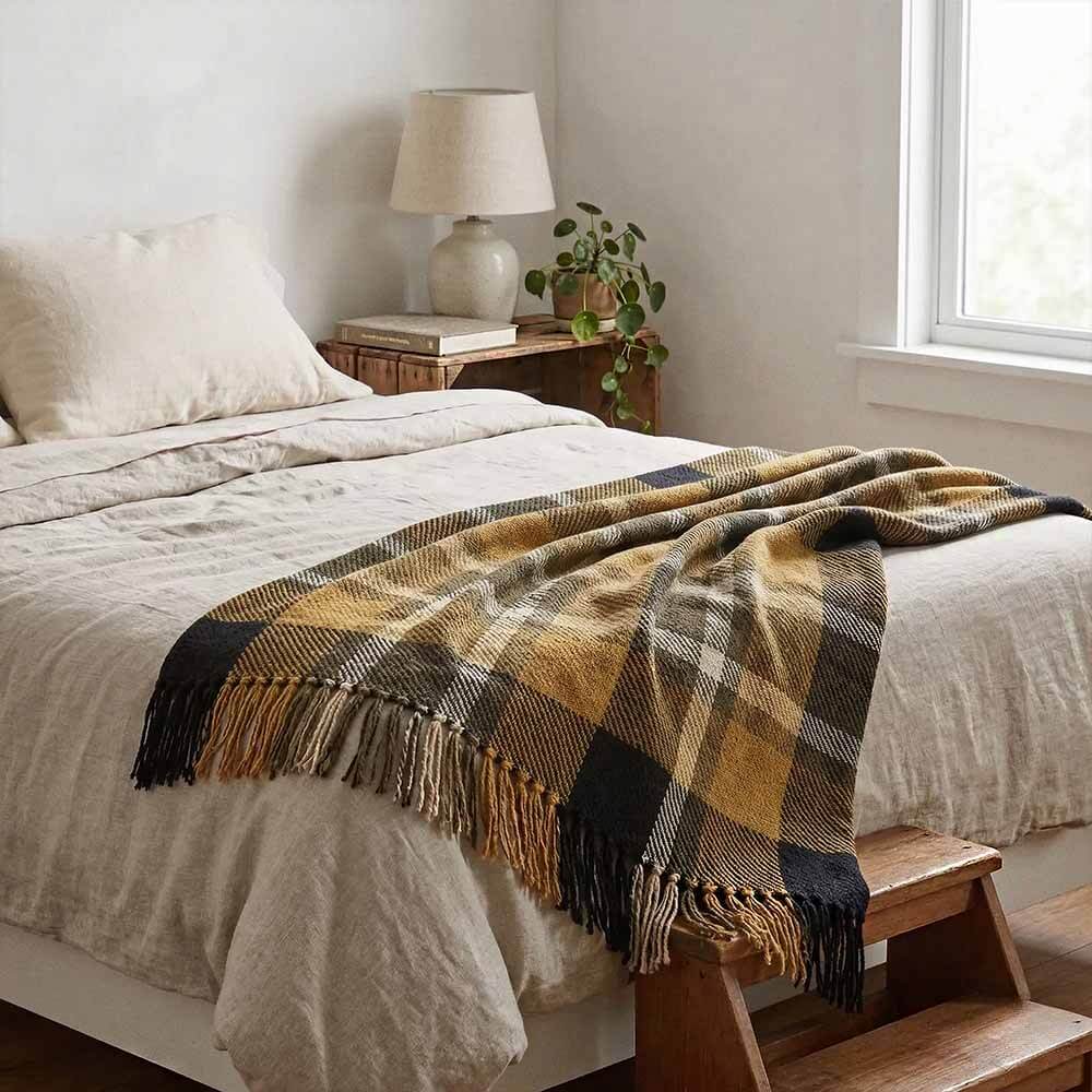 Yellow and Black Plaid Throw Blanket with Fringe 3 A yellow and black plaid throw blanket with fringe edges layered at the foot of a bed with light beige linen sheets. A wooden step stool and a small bedside table with a lamp are nearby. throw blanket for couch ideas