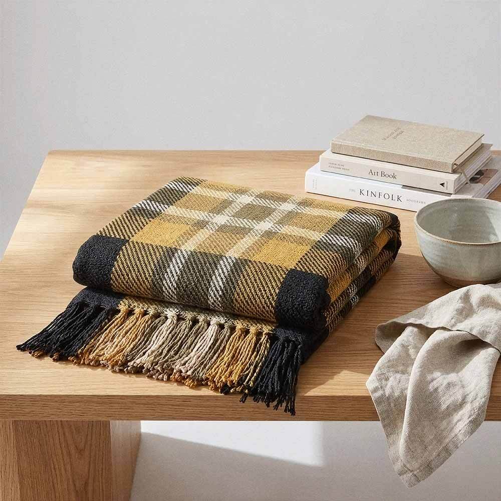 Yellow and Black Plaid Throw Blanket with Fringe 4 A neatly folded yellow plaid throw blanket resting on a light wooden table next to a stack of books and a small ceramic bowl. The focus is on the thick cotton weave and the hand-tied fringe. throw blankets for bed