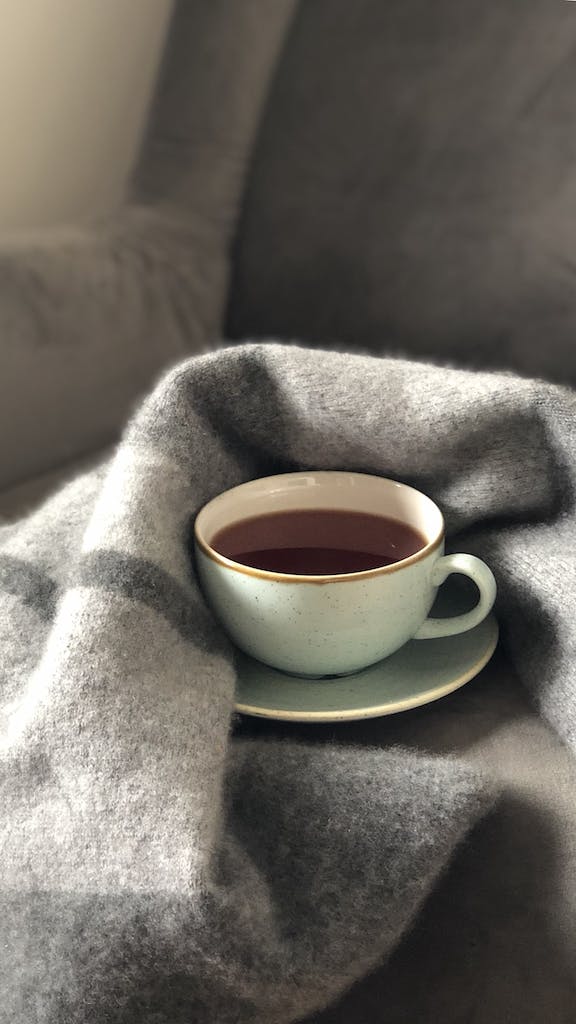 White Ceramic Cup on Saucer surrounded by a throw blanket