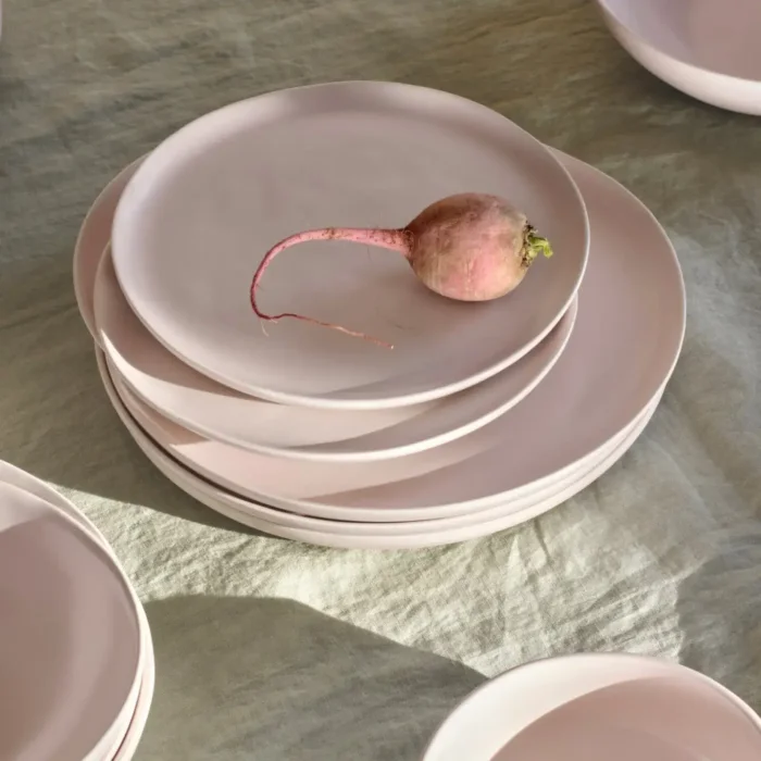 Fable Small Plates A stack of Fable Small Salad Plates in a soft pink hue, with a single radish on top, highlighting their simple elegance.