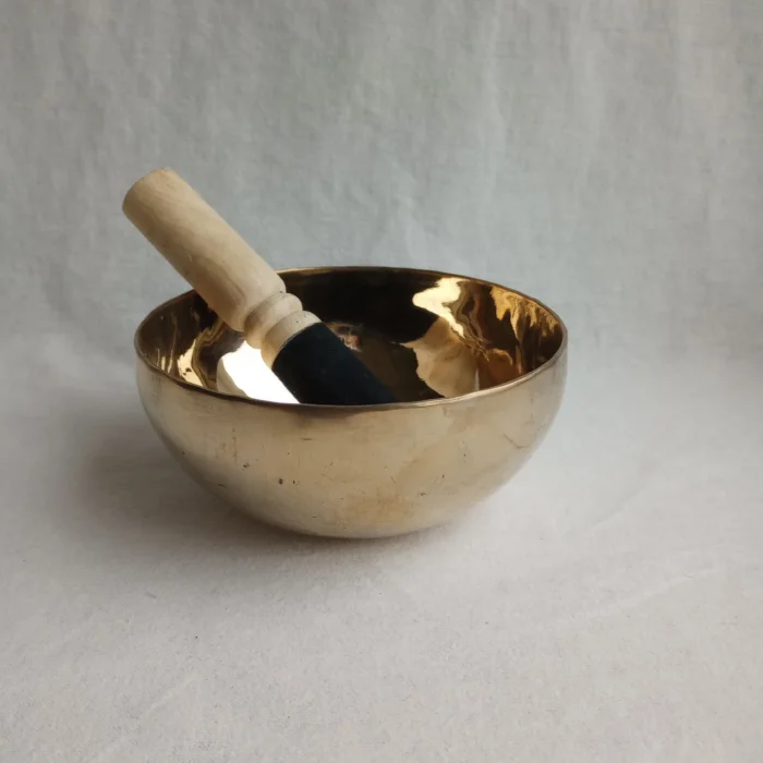 Close-up of the Metal Singing Bowl with the wooden mallet resting on its side, highlighting the shiny surface.