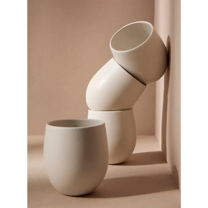 A set of four white GHARYAN Stoneware Coffee Mugs, arranged in a unique, balanced stack against a neutral background.