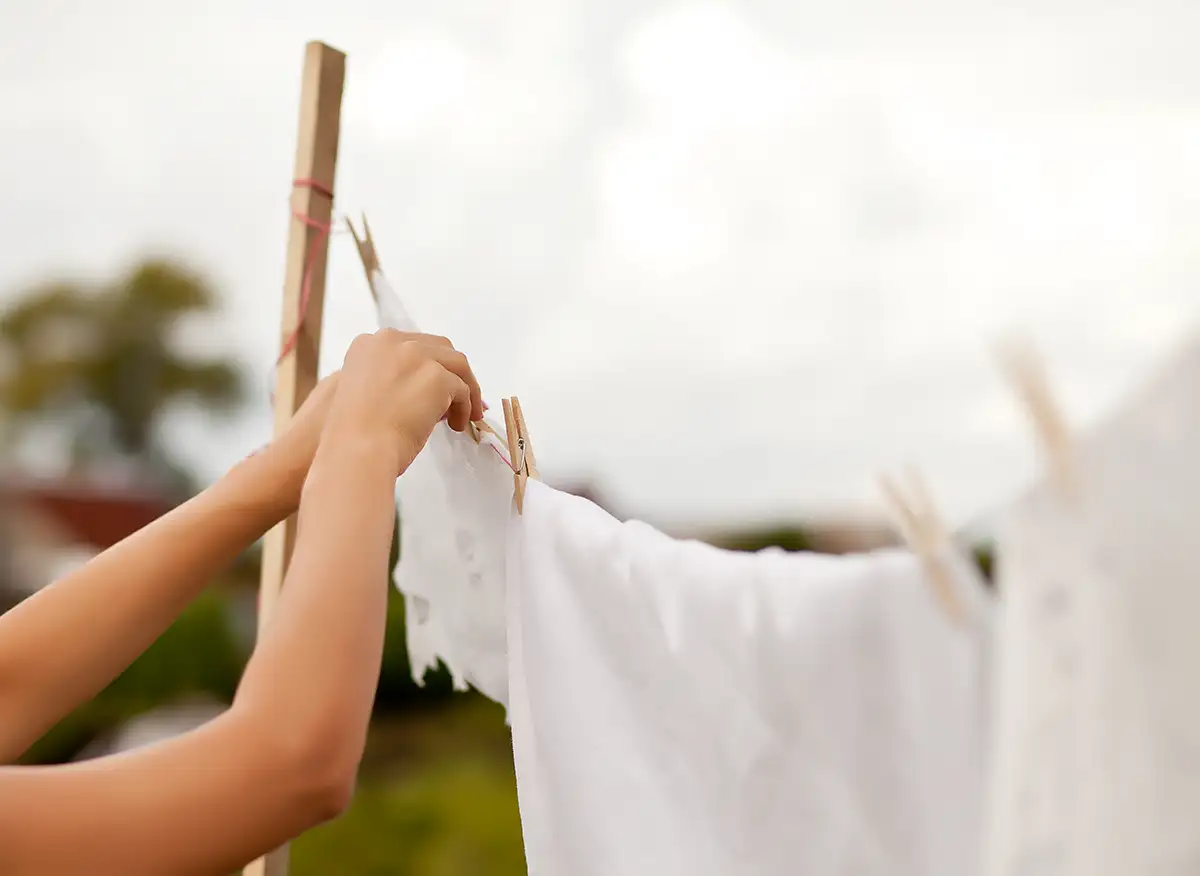 The Benefits of Using Essential Oils in Your Laundry 1 Person hanging white clothes on a clothesline outdoors. Benefits of using essential oils in your laundry.