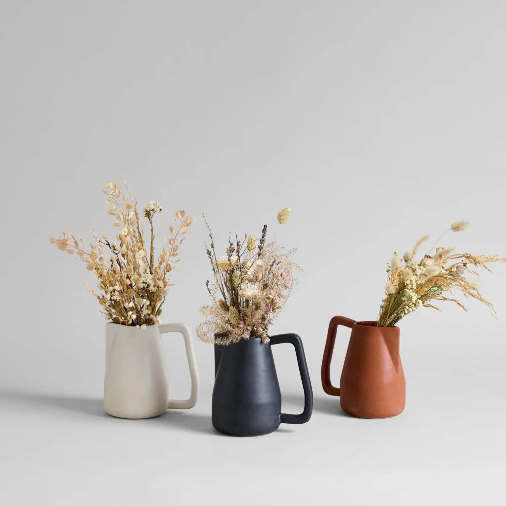Is Handmade Pottery Microwave Safe? 9 Three ceramic pitchers in white, black, and terracotta colors, each holding dried flowers.