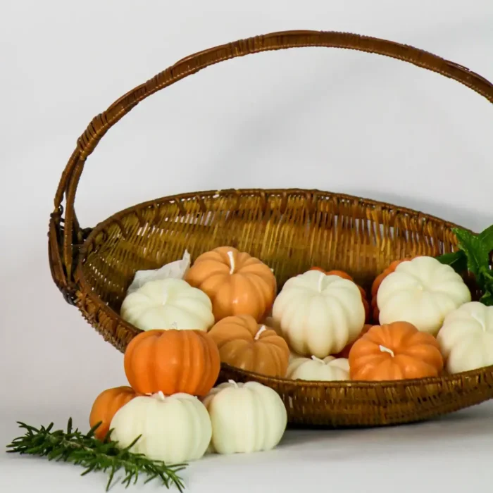 A brown wicker basket filled with orange and white Pumpkin Scented Candles on white background