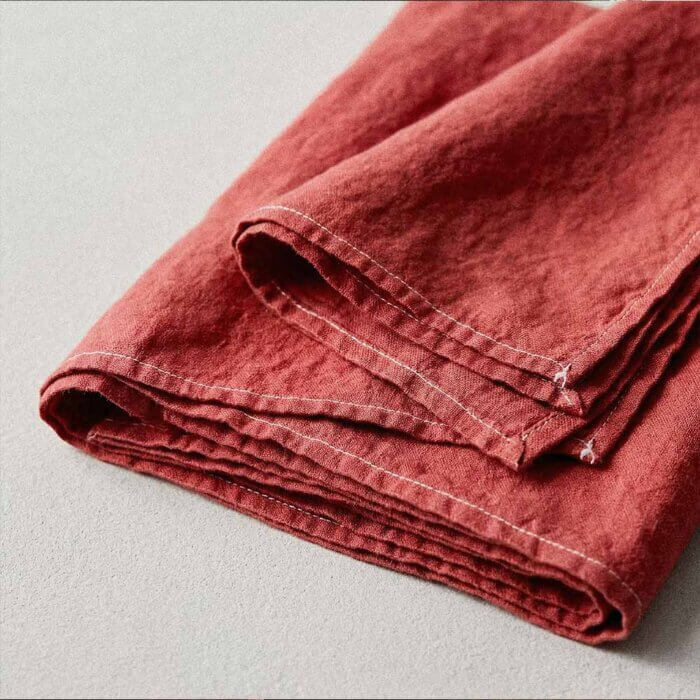 Red coral linen tablecloth handmade in USA folded showing prewashed pure linen texture with cream topstitched edge