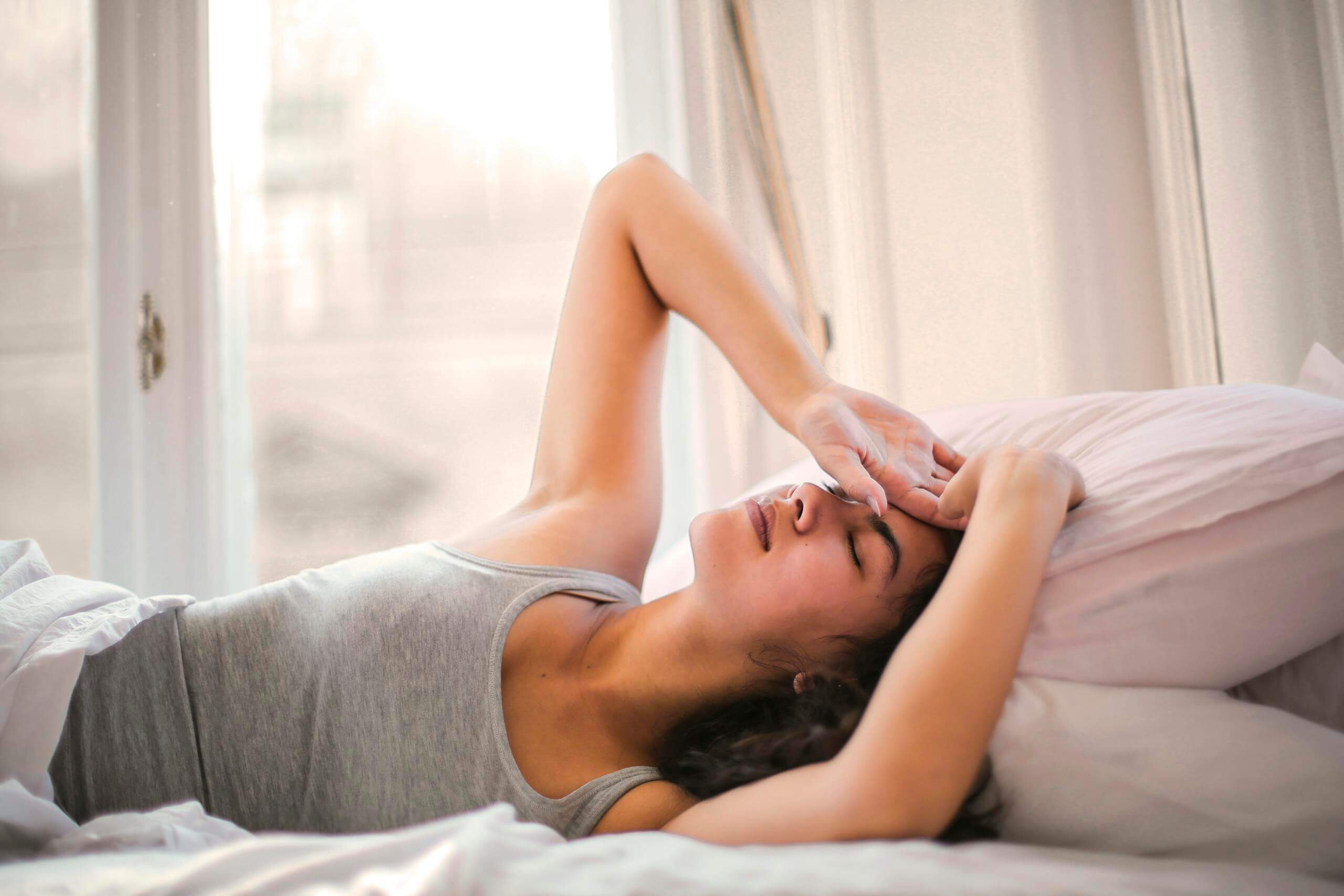 How Light Pollution Affects Sleep and 10 Ways to Fix It (2024 Guide) 1 Woman in Gray Tank Top Lying on Bed. Light Pollution Affects Sleep