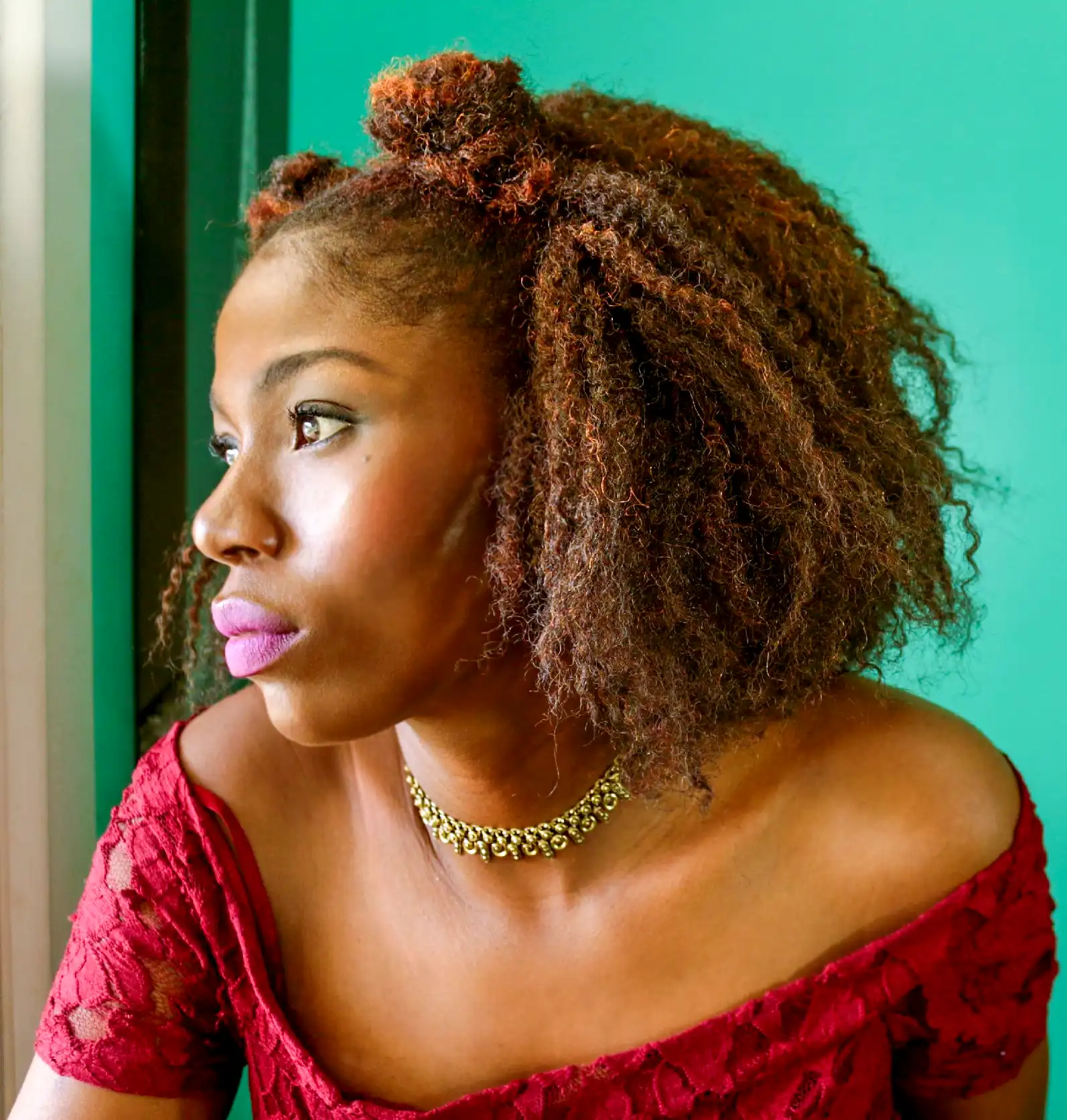 13 Must-Have Beauty Products for Every Woman 1 African American woman with big curly hair wearing a lace red dress in front a window. Must-Have Beauty Products for Every Woman