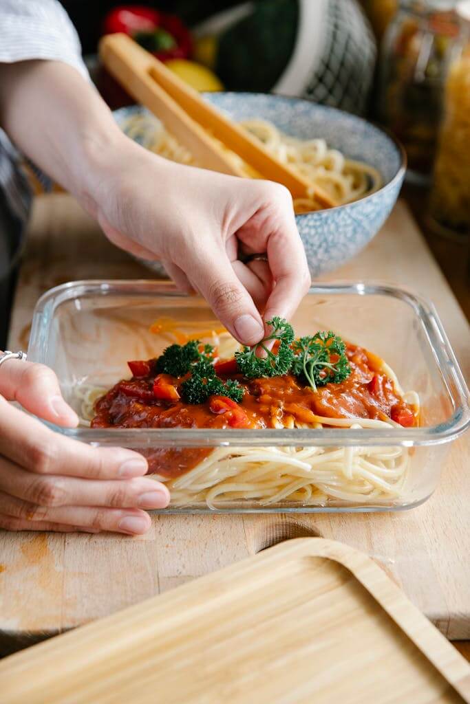 The Healthiest Material for Cookware| Your Guide to the Best Materials for Pots & Pans in 2025 11 Crop anonymous cook putting green parsley into glass container with pasta and tasty bolognese sauce while cooking at kitchen counter