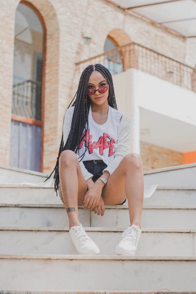 Gen Z sustainability | Intentions vs. Reality: The Sustainability Say-Do Gap in 2025 3 gen z sustainability influencers. Fashionable young woman posing confidently on urban stairs with sunglasses and braids.