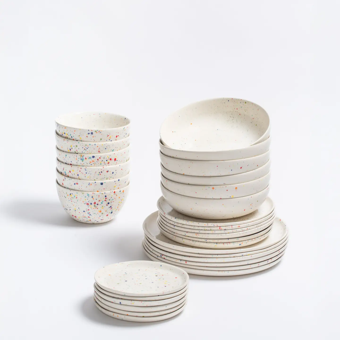 16-Piece White Ceramic Dishes Set | Made In Portugal 1 White Ceramic Dinnerware. A stack of 16 white ceramic dishes including dinner plates, salad plates, pasta plates, and bread plates. Each piece is decorated with bright, colorful confetti speckles like a celebration