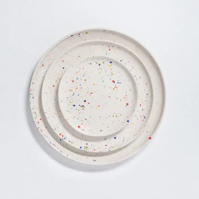 Top-down view of three round white ceramic plates in different sizes. The organic, wavy edges show the handmade Portuguese craftsmanship, and colorful dots are scattered across the white surface. colorful dishe sets