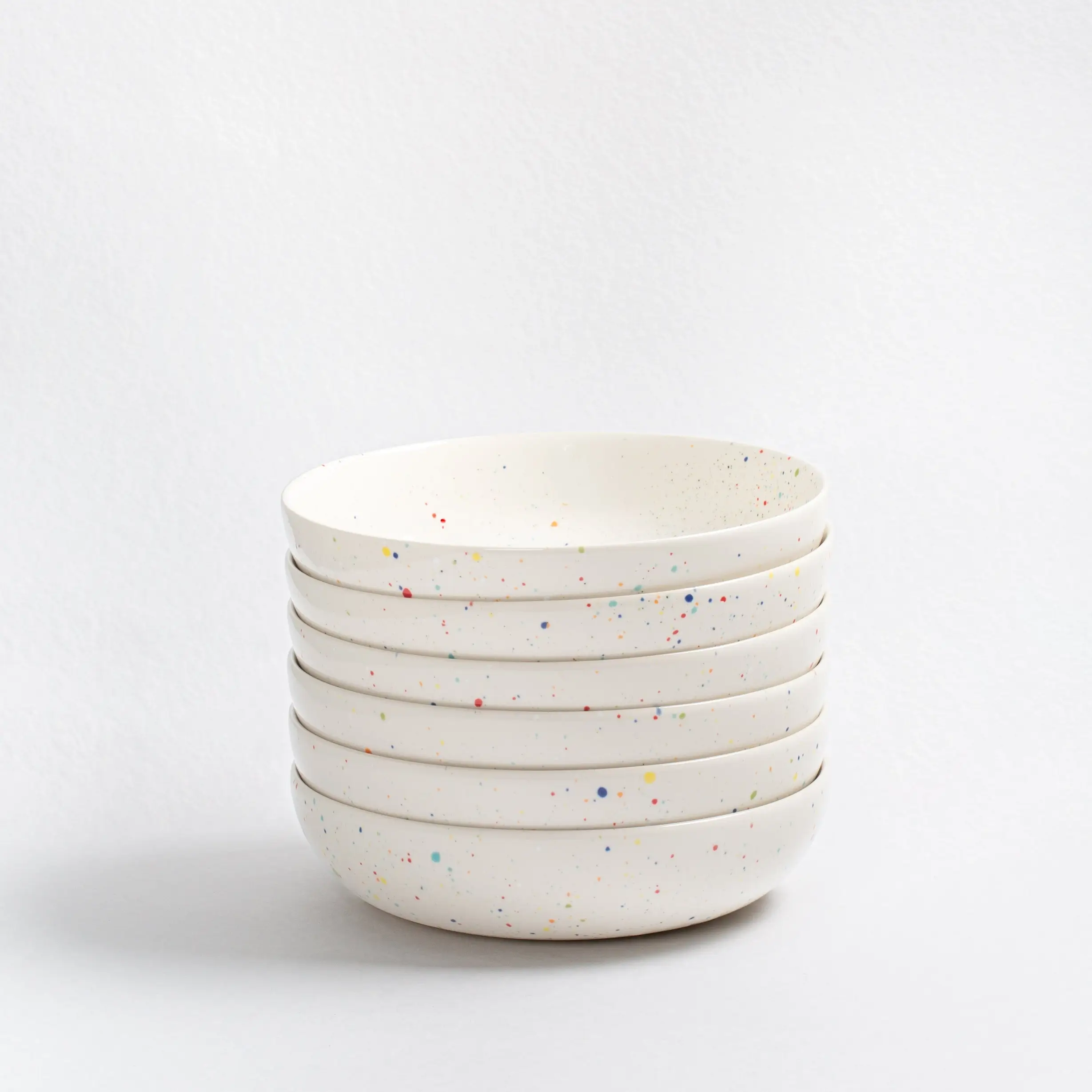 16-Piece White Ceramic Dishes Set | Made In Portugal 4 White Ceramic Dishes Set. A tall, sturdy stack of four deep white stoneware bowls with colorful red, blue, and yellow speckles. The bowls have a smooth, glossy finish and natural, non-perfect edges. dinnerware sets for 12 with serving pieces