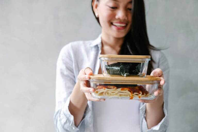15 Non Toxic Kitchen Essentials for a Safer, Eco-Friendly Kitchen 3 Smiling Asian woman holding two bento boxes filled with delicious food indoors.