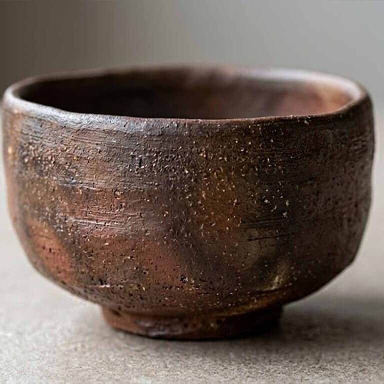 What Is a Chawan? A Guide to the Japanese Matcha Bowl 7 A traditional Japanese Bizen chawan tea bowl, hand-shaped with an organic, slightly uneven form, completely unglazed surface, rich earthy clay tones ranging from deep brown to reddish hues, natural fire markings created by ash and flame